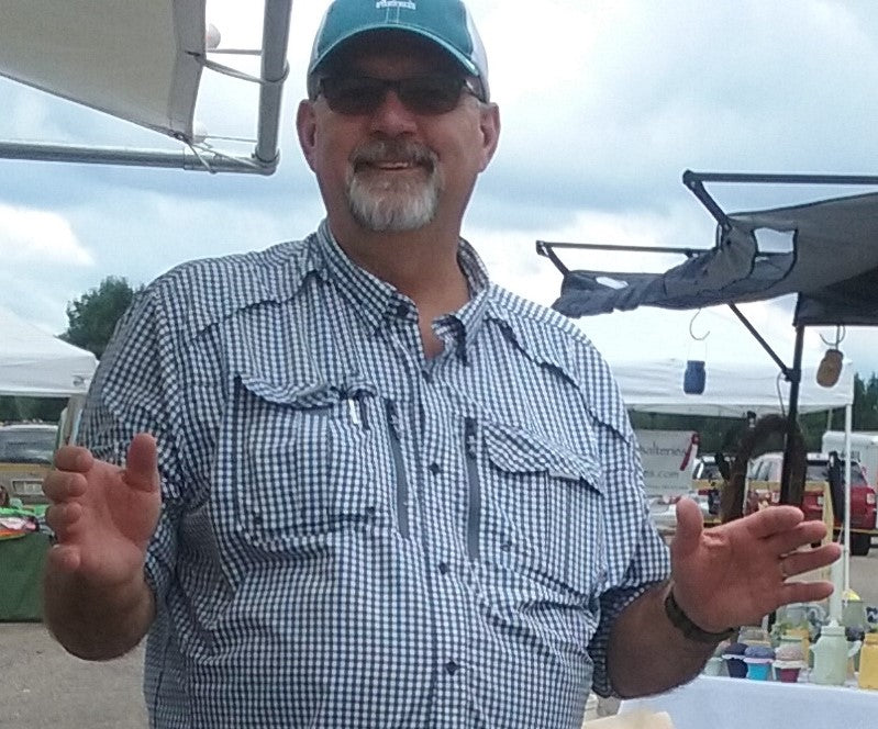 Man wearing a checkered shirt and cap with sunglasses, standing outdoors.