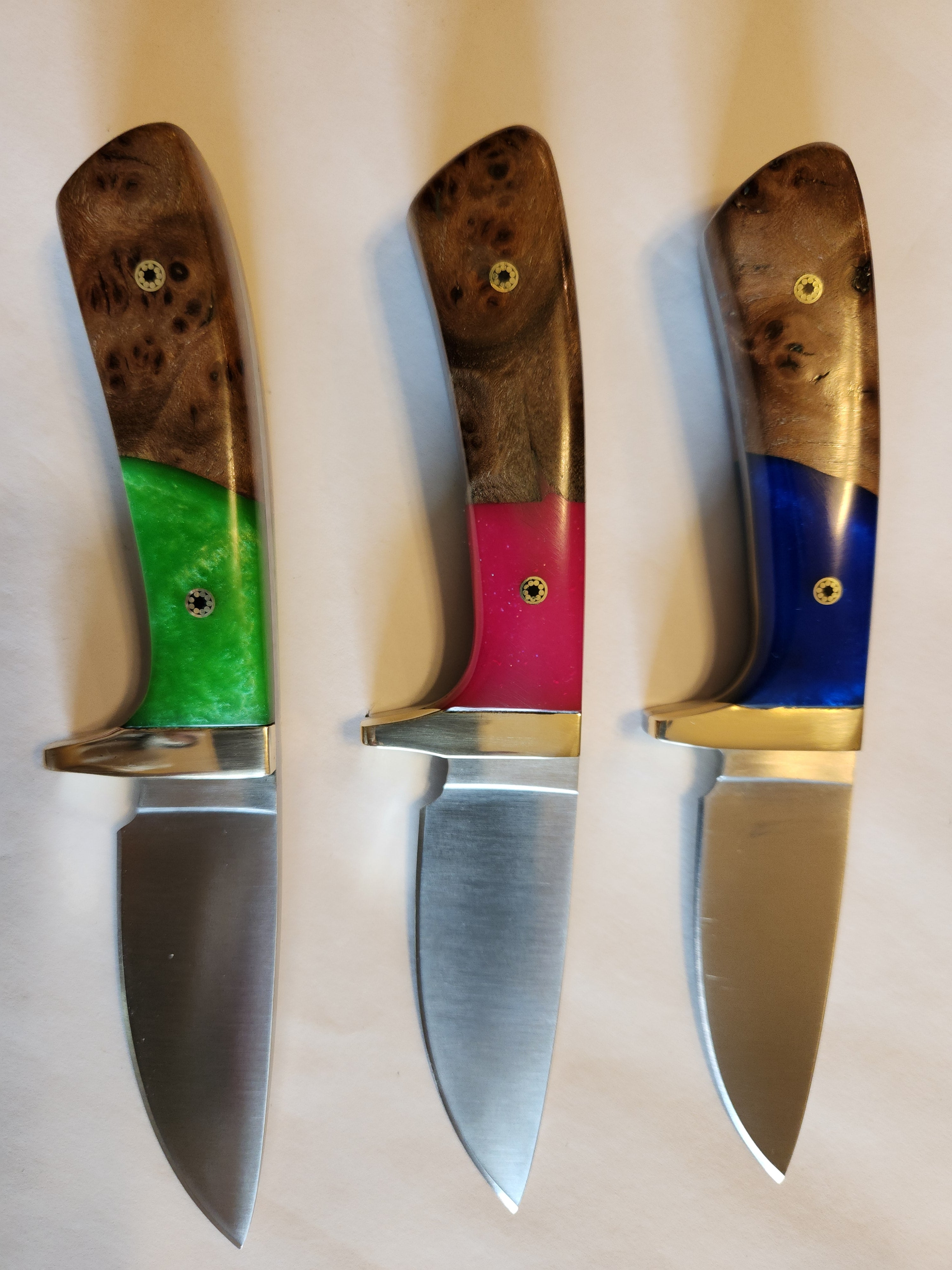 Three knives with colored handles on a beige background, custom made by KCK for Steve M